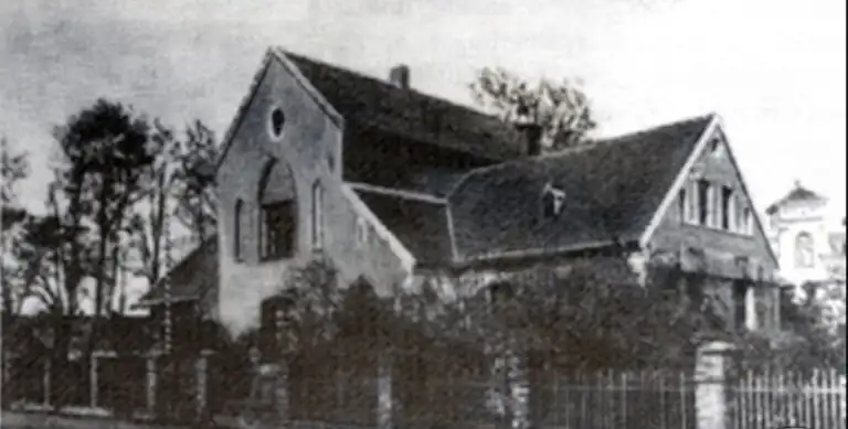 Budynek dawnej szkoły ewangelickiej w Bogdanowie w okresie międzywojennym, już pozbawiony wieżyczki. W tle widoczny kościół.